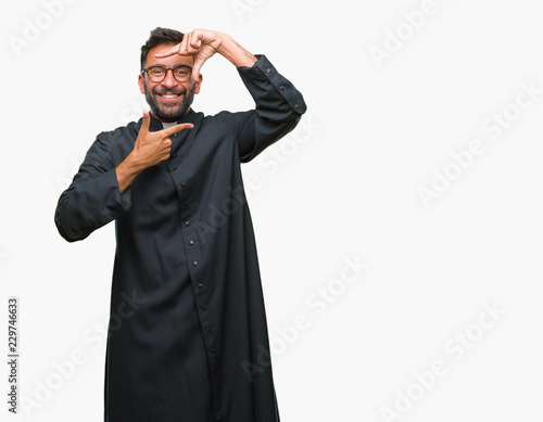 Adult hispanic catholic priest man over isolated background smiling making frame with hands and fingers with happy face. Creativity and photography concept.