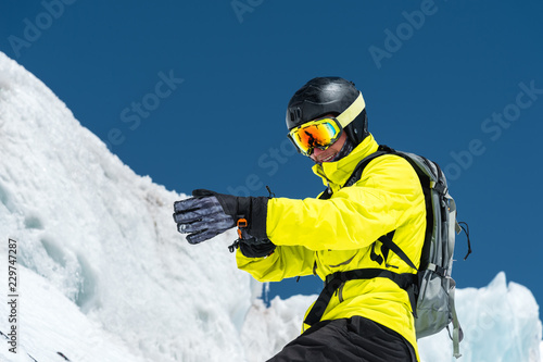 Professional skier in a helmet with a backpack and a ski mask standing on a glacier is preparing to jump wearing membrane gloves. The concept of quality training for the sport