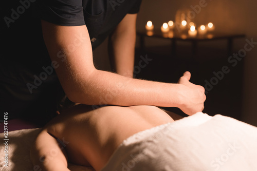 Close-up Spa massage low angle. male massage therapist doing a back and shoulder massage to a young girl with her elbows in a dark office amid burning candles