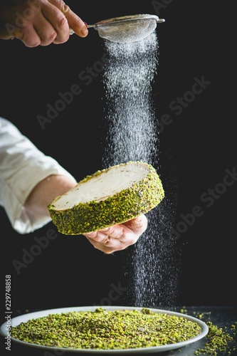 Confectioner dusting small pistachio cake with powdered sugar photo