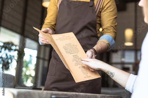 cropped shot of waiter showing menu list to female customer in cafe