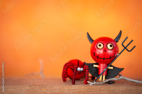 Happy red devil doll and red spider over blurred orange background, Halloween decoration item concept