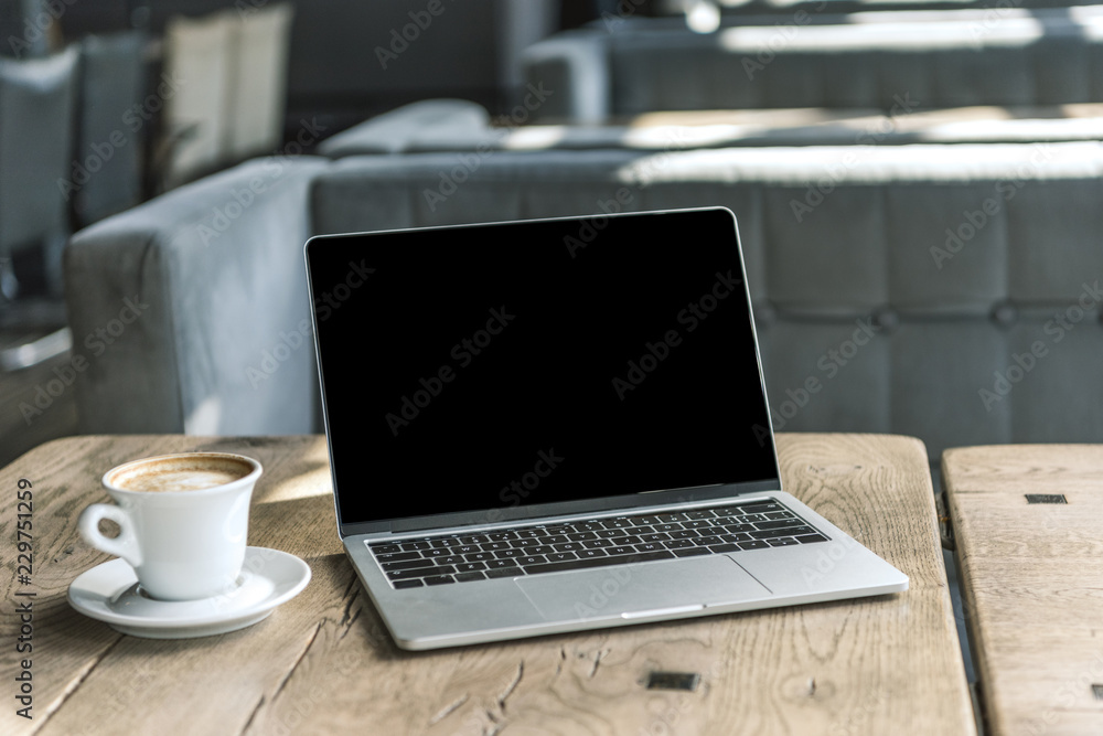 Fototapeta premium cup of coffee and laptop with blank screen on rustic wooden table at cafe