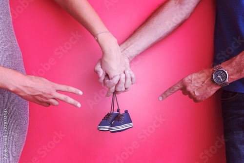 young pregnant couple holding newborn baby shoes