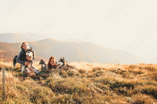 Two girl in the top of mount play with two husky. Ukrainian Carpathians in autumn time. Warm colored green leaves.Forests and mountains view. Travel with dog.