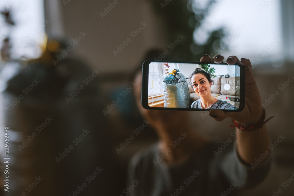 Woman taking selfie in living room. Selective focus on smart phone.