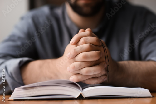 Religious young man with Bible praying at home, closeup