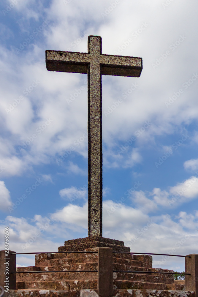The Cruz Alta viewpoint is the higest point in the Bussaco range in Portugal. The cross monument is under a blue sky with white clouds.