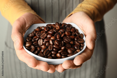 Woman holding bowl with coffee beans, closeup