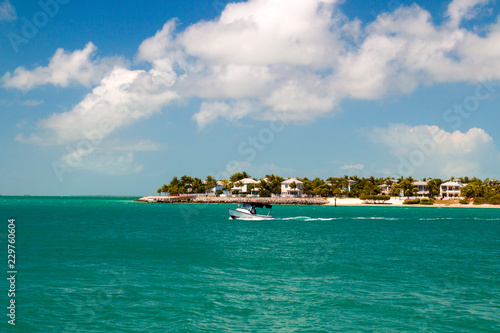 Tropical turquoise blue waters of the Sunset Key resort island in the city of Key West, boat on sea, sandy beach, palm trees, luxury beachfront houses perfect holiday, Florida.