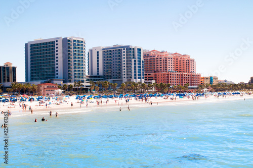 Tropical sandy beach vacation city Clearwater Beach in Florida, colourful beachfront hotel resorts buildings, palm trees, sunbathing tourists, turquoise blue sea waters of Mexican Gulf
