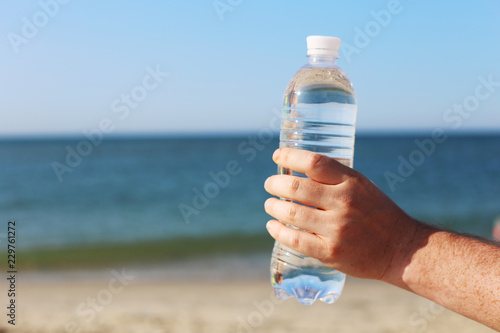 bottle of mineral water in hand with blue sea and beach background