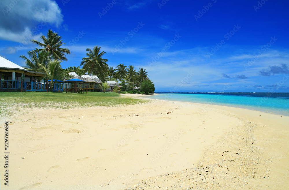 White golden sandy beach and coral blue sea waters with Polynesian beach front houses- traditional fale in Samoa Manase Beach in Pacific Ocean