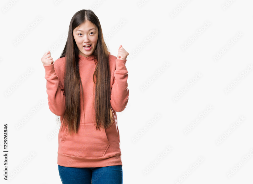 Young Chinese woman over isolated background wearing sport sweathshirt celebrating surprised and amazed for success with arms raised and open eyes. Winner concept. Young Chinese woman over isolated background wearing sport sweathshirt celebrating surprised and amazed for success with arms raised and open eyes. Winner concept.