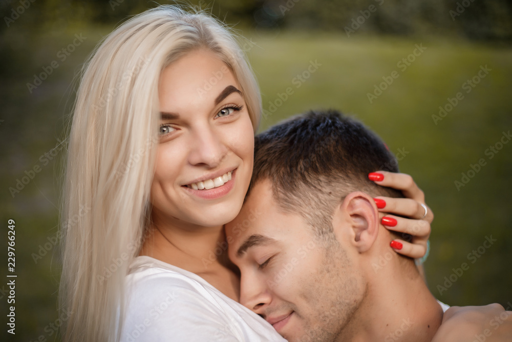 Loving couple standing on grass in nature green park with beautiful sundown light hugging. Man lies on woman's breast. Loving couple standing on grass in nature green park with beautiful sundown light hugging. Man lies on woman's breast.