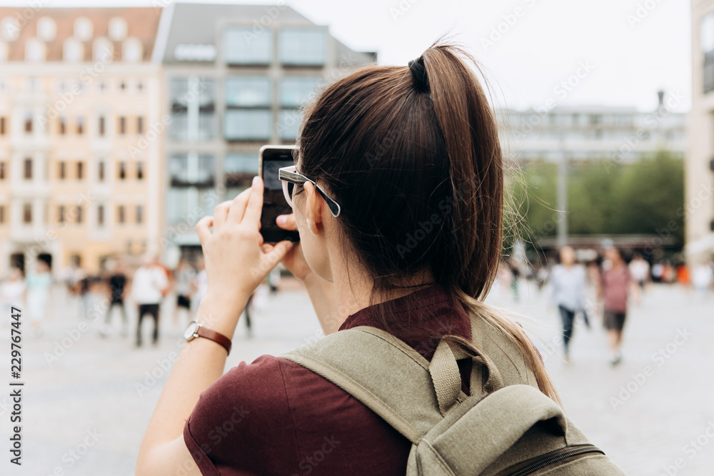 The girl on the street takes pictures of the beautiful buildings in Leipzig in Germany. She makes a street mobile photo to share it on social networks with friends.