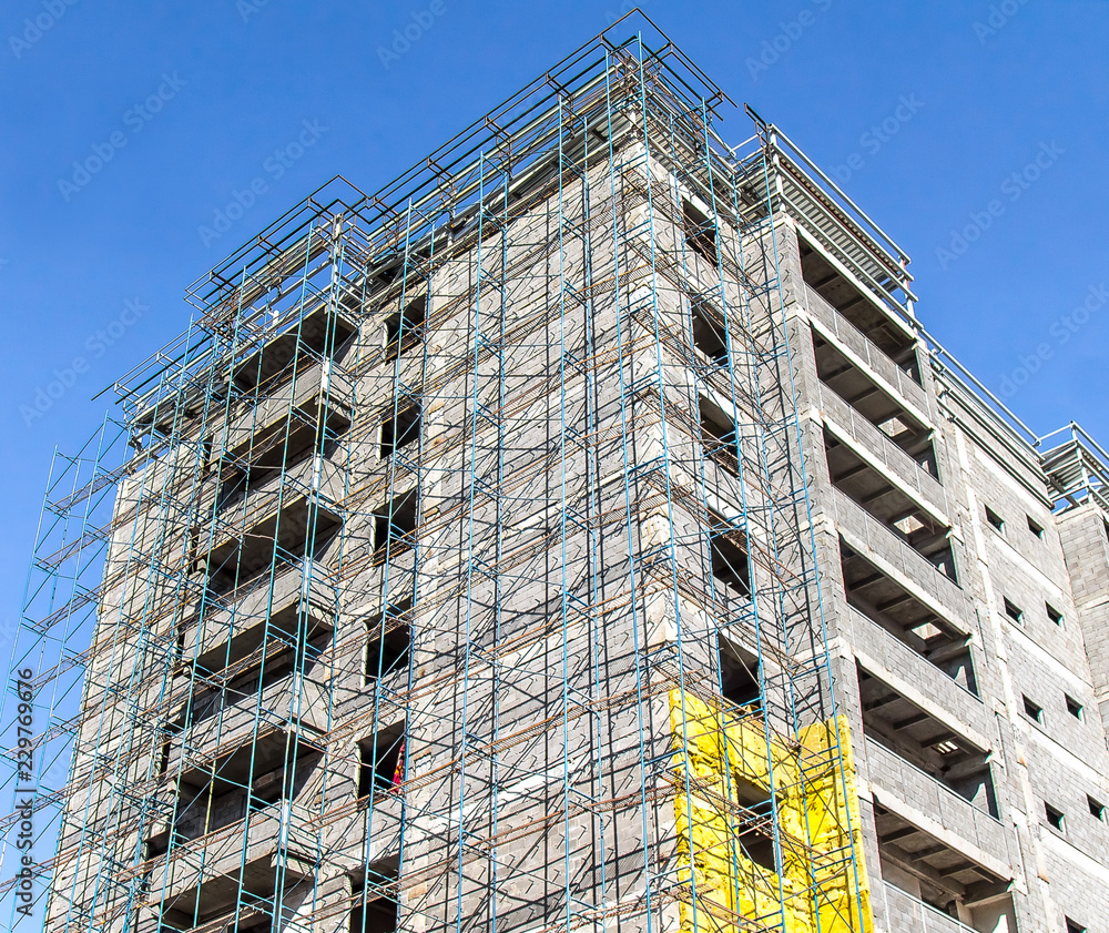 Building under construction in scaffolding on the sky background