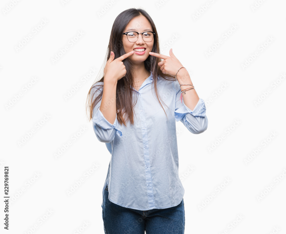Young asian business woman wearing glasses over isolated background smiling confident showing and pointing with fingers teeth and mouth. Health concept. Young asian business woman wearing glasses over isolated background smiling confident showing and pointing with fingers teeth and mouth. Health concept.