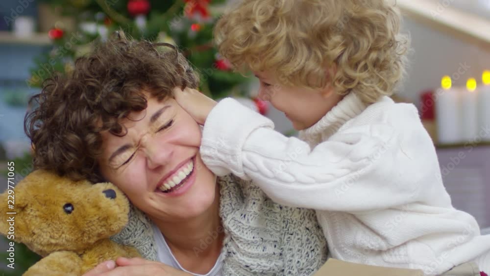 Handheld shot of adorable playful little boy with curly hair kissing laughing mother in temple on Christmas day Handheld shot of adorable playful little boy with curly hair kissing laughing mother in temple on Christmas day