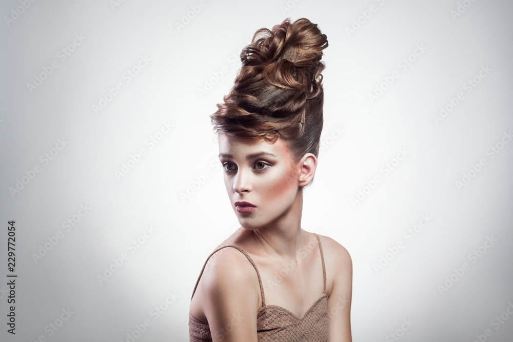 portrait of attractive brunette woman with stylish hairdo and makeup wearing beige singlet looking aside on isolated grey background. indoor, studio shot on copy space.