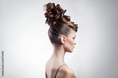 side view of attractive brunette woman with stylish hairdo and makeup posing on isolated grey background. indoor, studio shot on copy space.