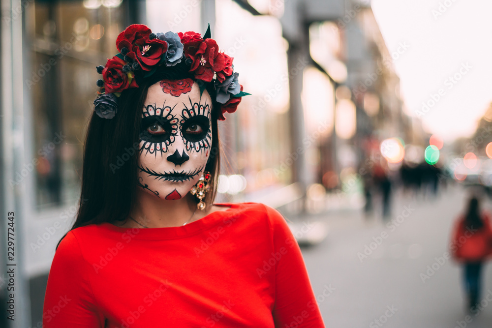 a man with a painted face of a skeleton, a dead zombie, in the city during the day. day of all souls, day of the dead, halloween, ghost walk.