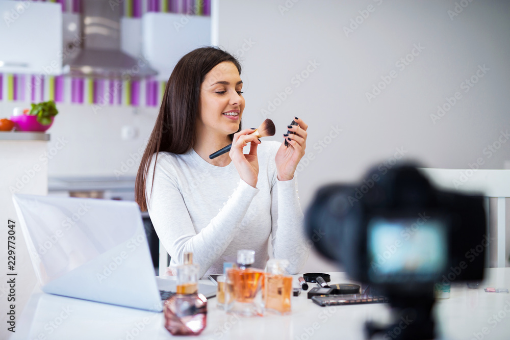 Young cute blogger woman filming her presentation of cosmetic products. Sitting in a bright room in front of camera. Young cute blogger woman filming her presentation of cosmetic products. Sitting in a bright room in front of camera.