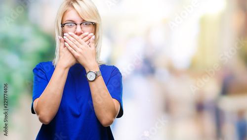 Young beautiful blonde woman wearing glasses over isolated background shocked covering mouth with hands for mistake. Secret concept. © Krakenimages.com