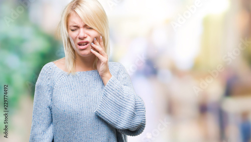 Young beautiful blonde woman wearing winter sweater over isolated background touching mouth with hand with painful expression because of toothache or dental illness on teeth. Dentist concept. © Krakenimages.com