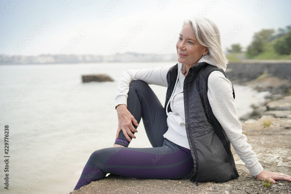  Beautiful elderly woman sitting by the ocean in sportswear