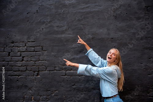 Happy young blonde pointing on a grey wall background