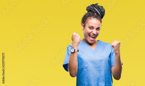 Young braided hair african american girl professional nurse over isolated background very happy and excited doing winner gesture with arms raised, smiling and screaming for success