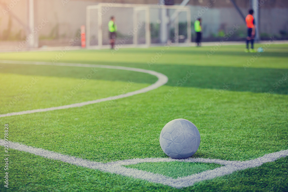 Obraz premium Ball on artificial turf at corner of football field with blurry player.