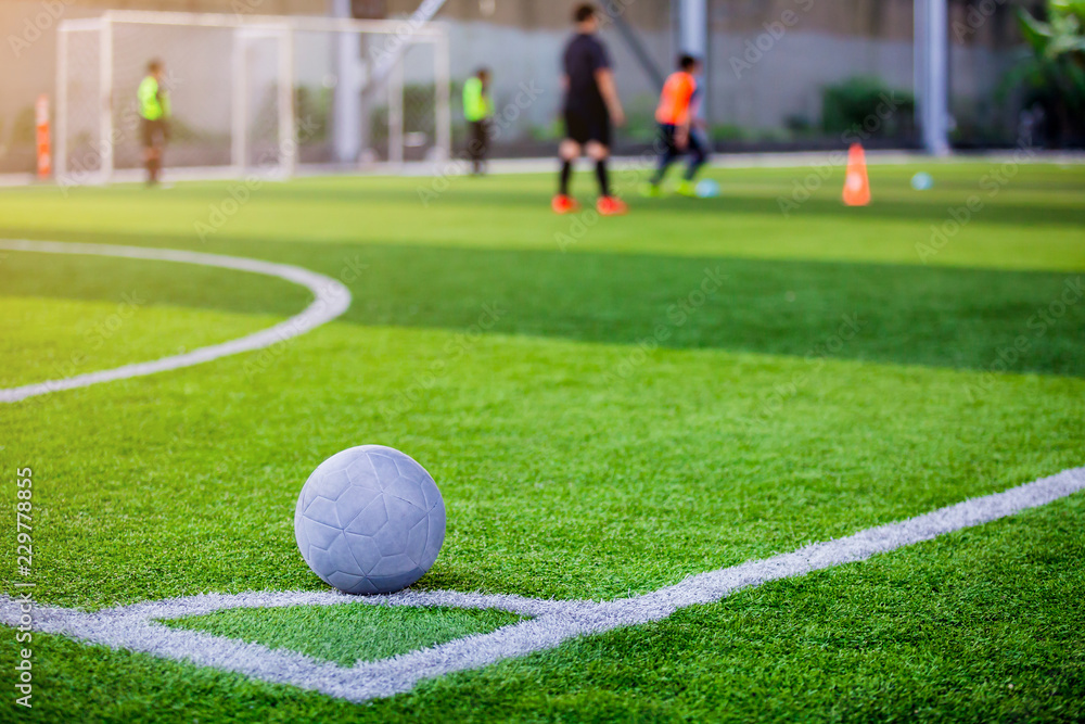Fototapeta premium Ball on artificial turf at corner of football field with blurry player.