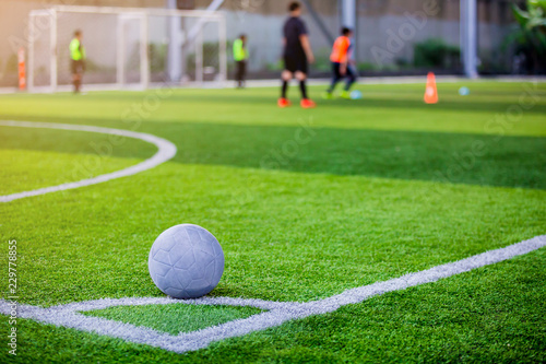 Ball on artificial turf at corner of football field with blurry player.