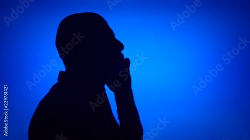 Silhouette of senior man using mobile on blue background. Male's face in profile talking on cellphone. Black contur shadow of grandfather's half-face