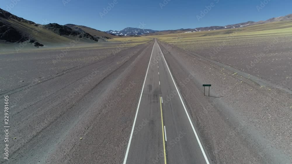 Aerial drone scene of road in desertic landscape with snowy colorful mountains. Rocky dry climate . Golden vegetation in surface. Flying fowards. Catamarca, Argentina Aerial drone scene of road in desertic landscape with snowy colorful mountains. Rocky dry climate . Golden vegetation in surface. Flying fowards. Catamarca, Argentina