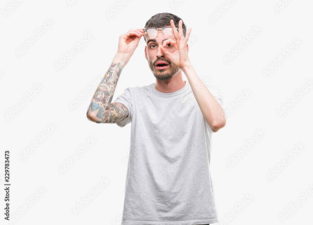 Young tattooed adult man doing ok gesture shocked with surprised face, eye looking through fingers. Unbelieving expression. Young tattooed adult man doing ok gesture shocked with surprised face, eye looking through fingers. Unbelieving expression.