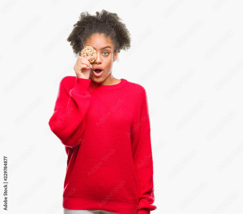 Young afro american woman eating chocolate cookie over isolated background scared in shock with a surprise face, afraid and excited with fear expression Young afro american woman eating chocolate cookie over isolated background scared in shock with a surprise face, afraid and excited with fear expression
