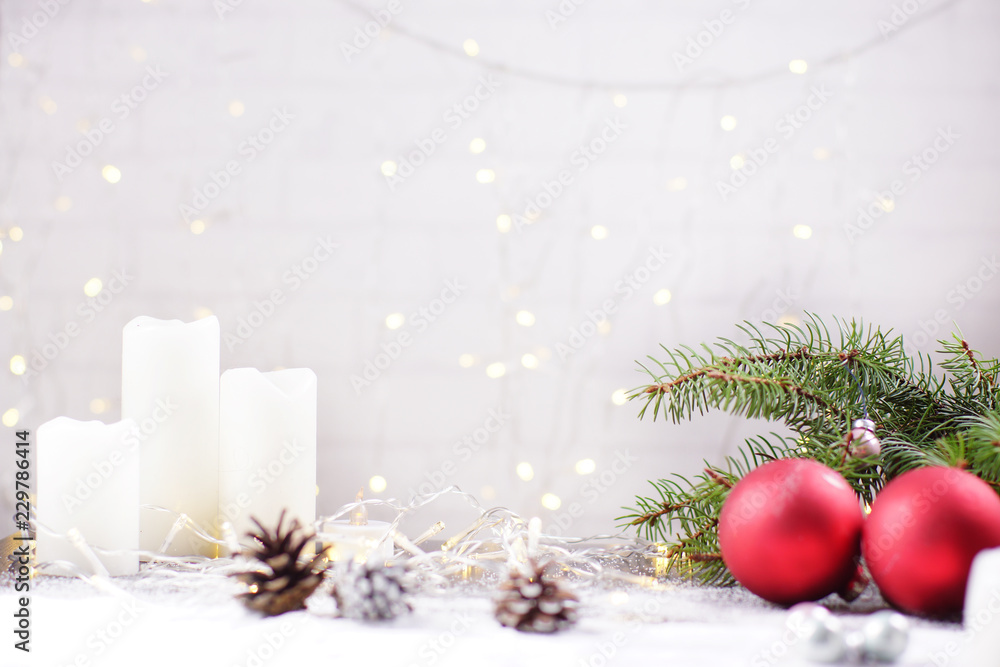 White background for a Christmas card, a wall with glowing garland, red Christmas balls and white candles on the table