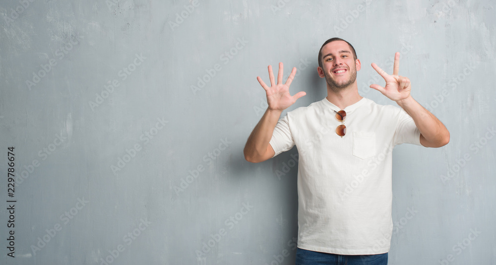 Young caucasian man over grey grunge wall wearing sunglasses showing and pointing up with fingers number eight while smiling confident and happy. Young caucasian man over grey grunge wall wearing sunglasses showing and pointing up with fingers number eight while smiling confident and happy.