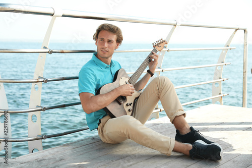 Portrait of handsome young man with guitar on sea pier