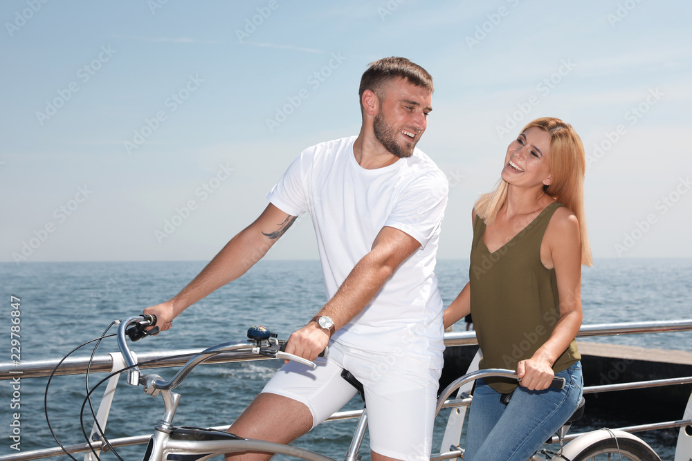 Couple riding tandem bike near sea on sunny day