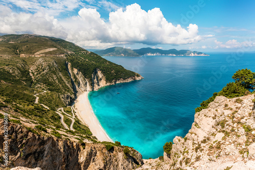 Myrtos beach on Kefalonia island at sunny day. Serpentine road on a green hill and turquoise Ionian Sea. 