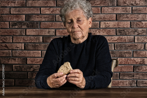 Foto Poor elderly woman with piece of bread at table