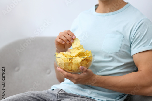 Foto Man with bowl of potato chips on grey sofa, closeup