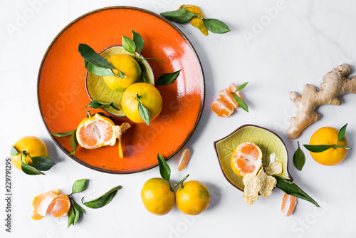 Fototapeta Naklejka Na Ścianę i Meble -  Still life in the style of flatlay. Ripe juicy tangerines against the background of an orange plate and a white background, with green foliage and ginger root.