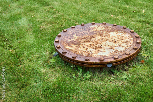 Rusty sewer manhole on green grass
