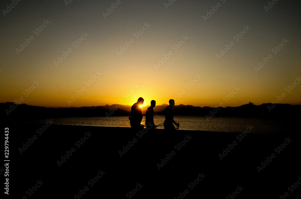 three men silhouette on the lagoon at sunset                               