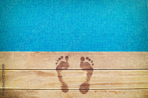 :icture of footprints on the wooden surface with blue swimming pool on the background photo